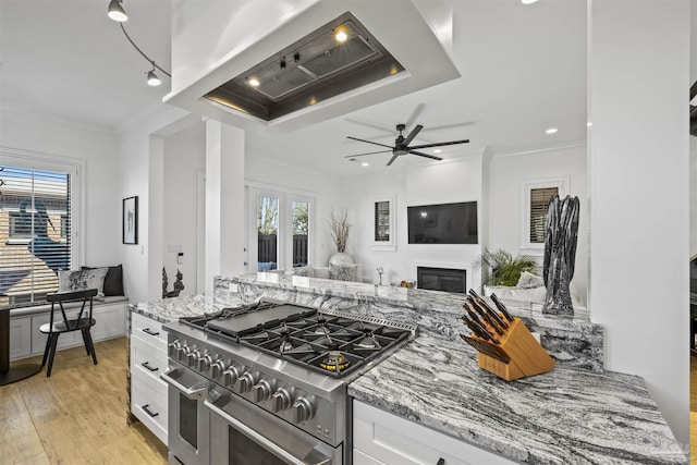 kitchen with white cabinetry, wall chimney range hood, light stone countertops, and range with two ovens