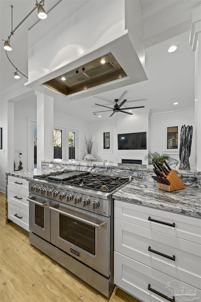 kitchen featuring white cabinetry, light stone counters, island range hood, and range with two ovens