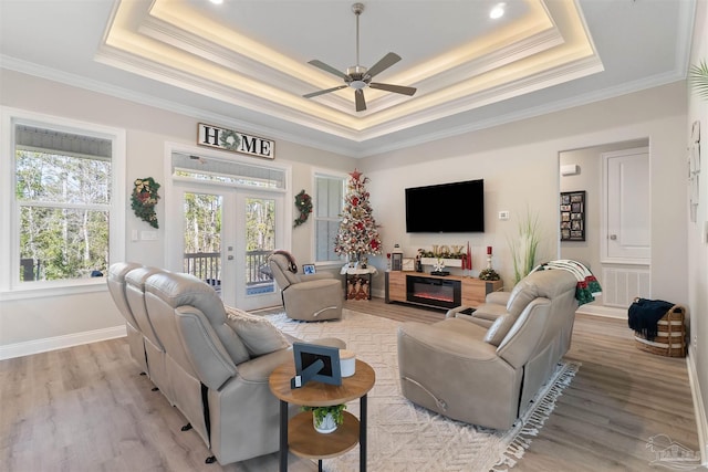 living room with ceiling fan, french doors, a raised ceiling, light hardwood / wood-style flooring, and crown molding