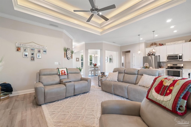 living room with a tray ceiling, light hardwood / wood-style flooring, ceiling fan, and crown molding