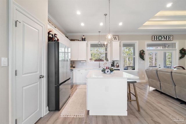 kitchen with white cabinets, ornamental molding, light hardwood / wood-style floors, appliances with stainless steel finishes, and a kitchen island