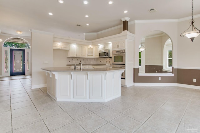 kitchen with light tile patterned flooring, white cabinetry, ornamental molding, appliances with stainless steel finishes, and an island with sink