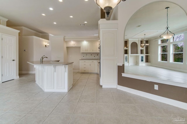 kitchen with crown molding, hanging light fixtures, light tile patterned floors, an island with sink, and decorative backsplash