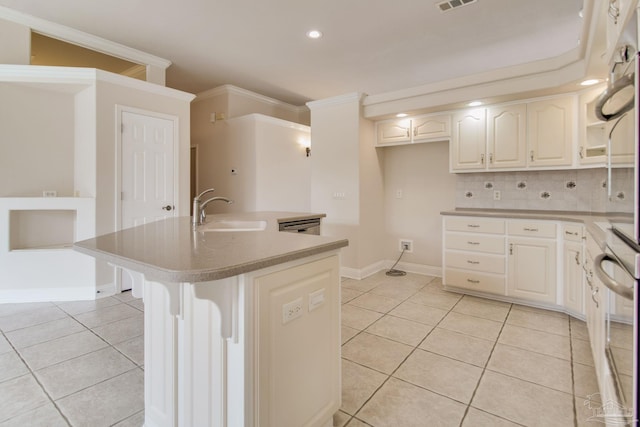 kitchen featuring sink, light tile patterned floors, ornamental molding, a kitchen island with sink, and backsplash