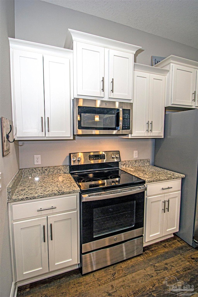 kitchen featuring white cabinets, light stone counters, stainless steel appliances, and dark wood-type flooring