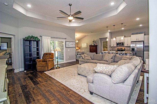 living room featuring a textured ceiling, a tray ceiling, ceiling fan, and dark wood-type flooring