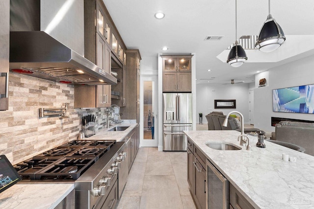 kitchen with pendant lighting, sink, wall chimney exhaust hood, appliances with stainless steel finishes, and light stone countertops