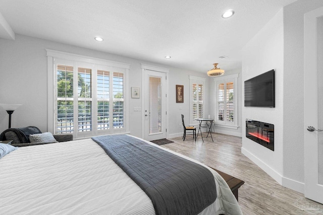 bedroom with multiple windows, access to outside, light hardwood / wood-style floors, and a textured ceiling