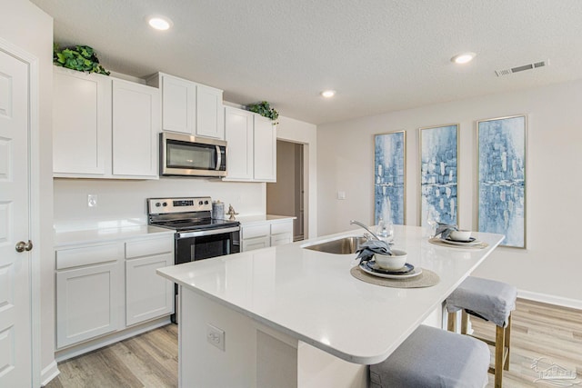 kitchen with sink, appliances with stainless steel finishes, a kitchen island with sink, white cabinetry, and a kitchen breakfast bar