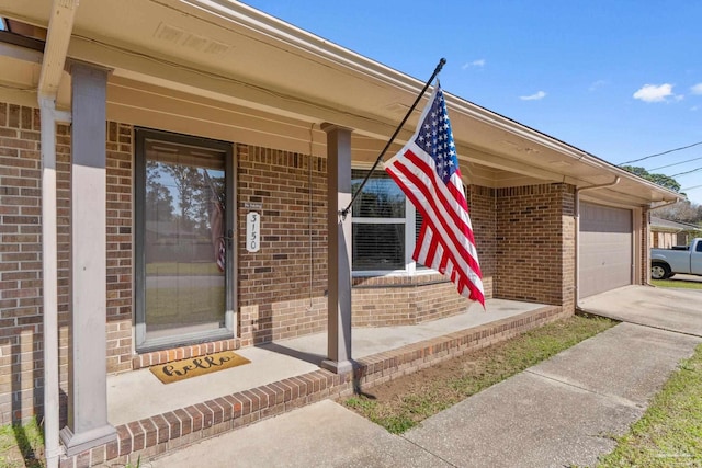 view of exterior entry with an attached garage, covered porch, concrete driveway, and brick siding