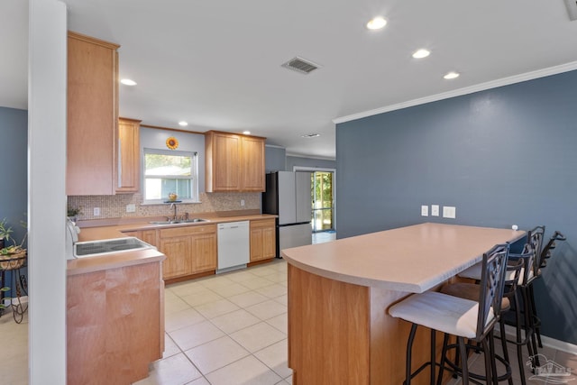 kitchen featuring white dishwasher, a peninsula, a sink, visible vents, and freestanding refrigerator