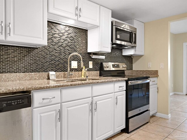 2701 E De Soto St, Pensacola, FL 32503 - kitchen with stainless steel appliances, a sink, light tile patterned floors, decorative backsplash, and white cabinets