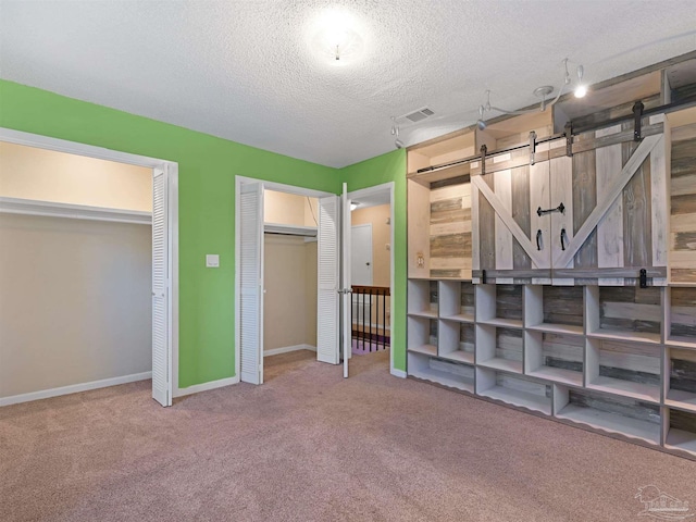 2701 E De Soto St, Pensacola, FL 32503 - unfurnished bedroom with multiple closets, carpet, a barn door, a textured ceiling, and baseboards