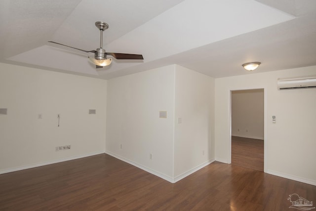 spare room featuring a raised ceiling, dark wood-type flooring, a wall mounted air conditioner, and ceiling fan