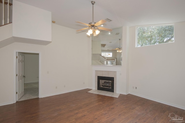 unfurnished living room featuring hardwood / wood-style flooring, ceiling fan, a tiled fireplace, and high vaulted ceiling