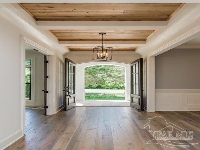entrance foyer with hardwood / wood-style flooring, beam ceiling, a chandelier, and ornamental molding