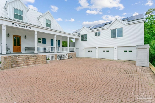 view of front of home featuring a porch, driveway, metal roof, roof mounted solar panels, and an attached garage