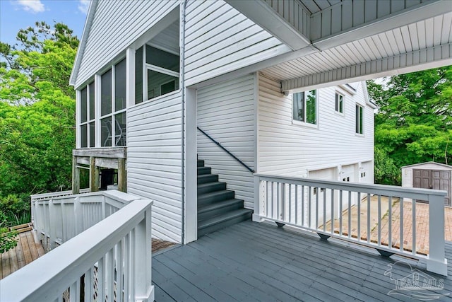 wooden deck with a storage unit, an attached garage, a sunroom, stairway, and an outbuilding