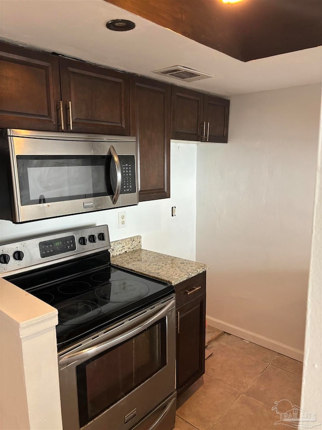 kitchen featuring stainless steel appliances, light stone counters, light tile patterned floors, and dark brown cabinetry