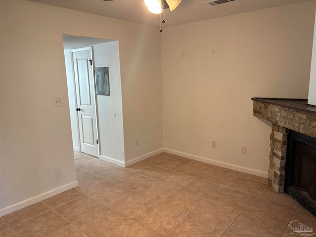 unfurnished living room featuring a stone fireplace, light tile patterned flooring, and ceiling fan