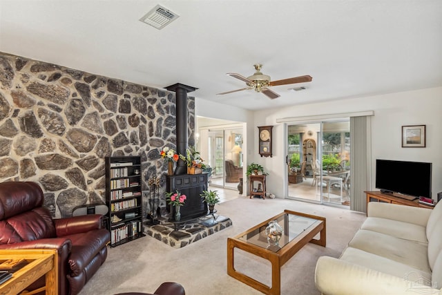 living room with a wood stove, light carpet, and ceiling fan