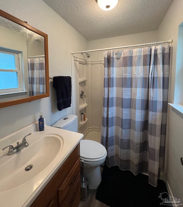 bathroom featuring a textured ceiling, toilet, vanity, and walk in shower