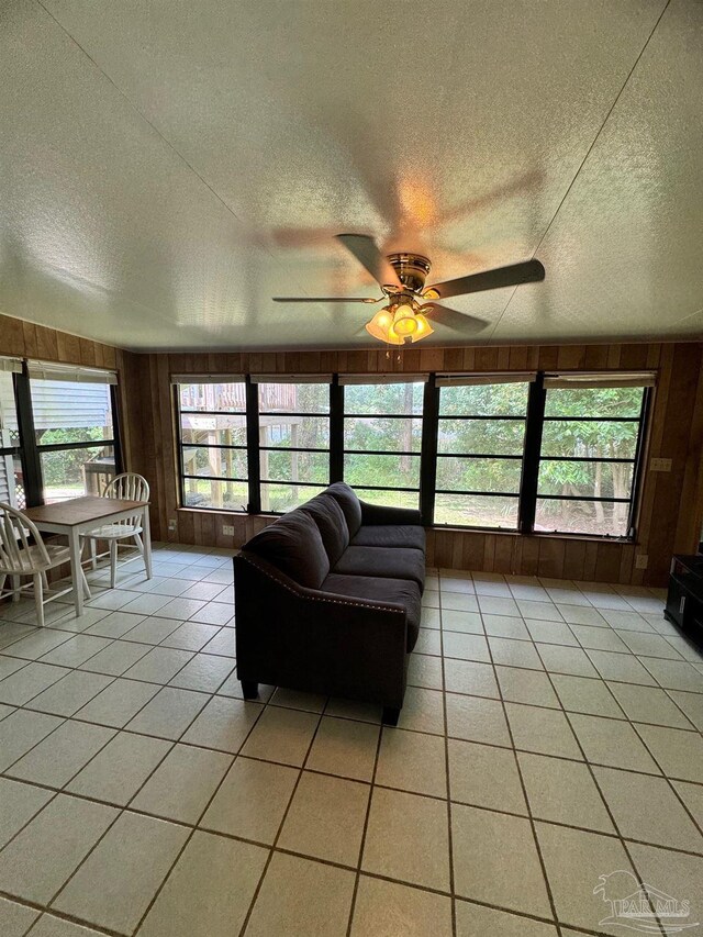 living room with a textured ceiling, wood walls, ceiling fan, and light tile patterned floors