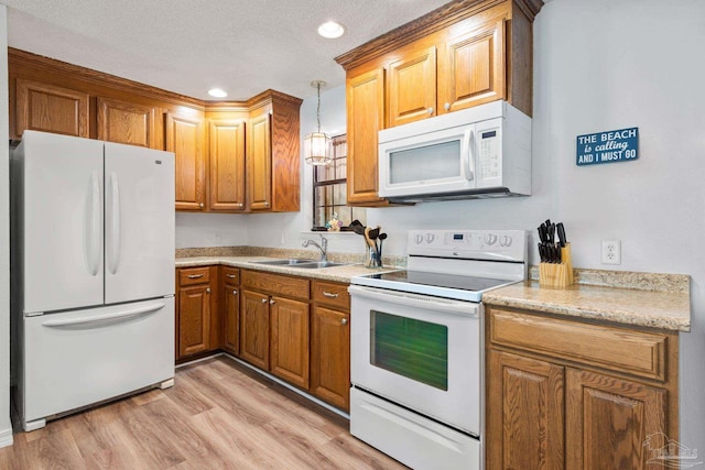 kitchen with white appliances, light wood-type flooring, a textured ceiling, decorative light fixtures, and sink