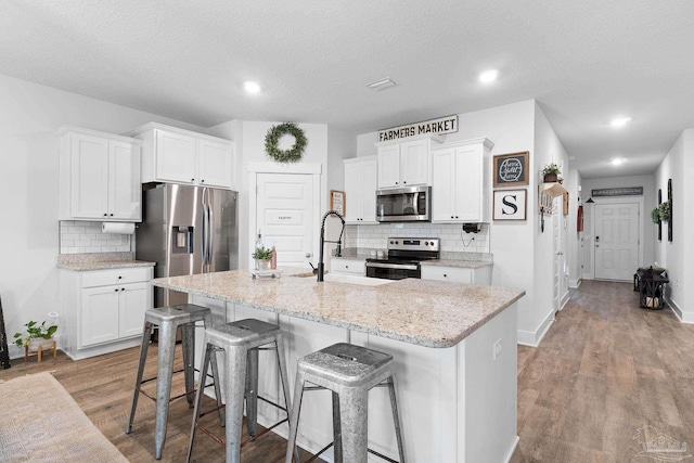 5722 Conley Ct, Pace, FL 32571 - kitchen featuring stainless steel appliances, decorative backsplash, a kitchen island with sink, a breakfast bar, and white cabinets