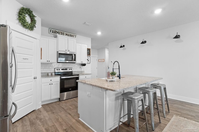 5722 Conley Ct, Pace, FL 32571 - kitchen with appliances with stainless steel finishes, light wood-style floors, a kitchen island with sink, light stone counters, and white cabinetry