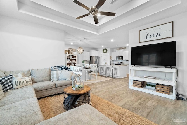 5722 Conley Ct, Pace, FL 32571 - living room featuring a raised ceiling, recessed lighting, ceiling fan, light wood-type flooring, and a chandelier