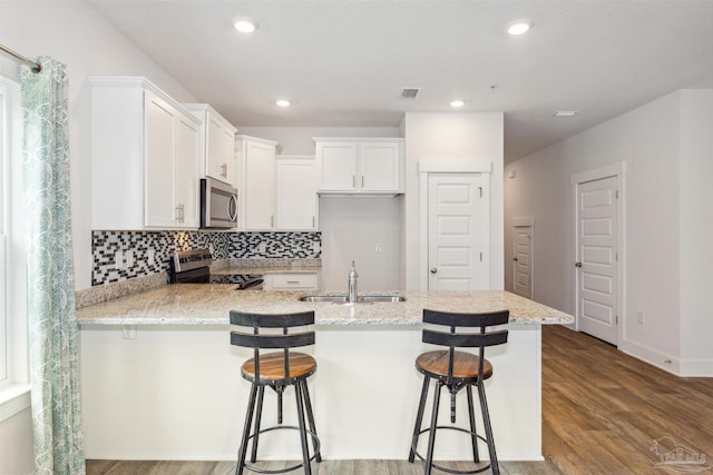 kitchen with sink, appliances with stainless steel finishes, a kitchen breakfast bar, light stone countertops, and white cabinets