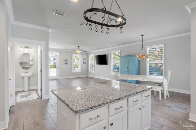 kitchen with white cabinets, ceiling fan with notable chandelier, a kitchen island, and plenty of natural light