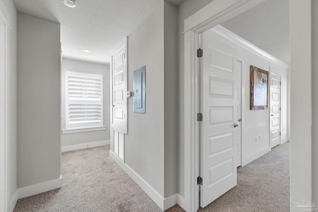 hallway featuring light colored carpet, a textured ceiling, and electric panel