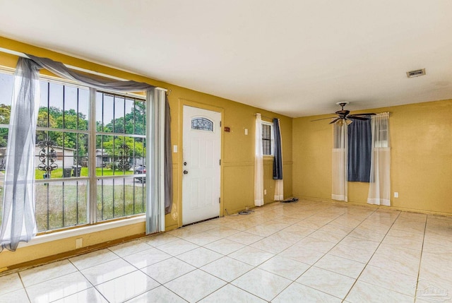 empty room featuring light tile patterned floors, visible vents, a ceiling fan, and baseboards