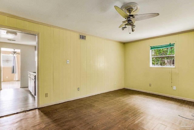 spare room with a ceiling fan, visible vents, crown molding, and wood finished floors