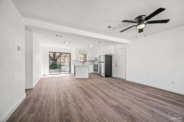 unfurnished living room with visible vents, a textured ceiling, baseboards, and wood finished floors