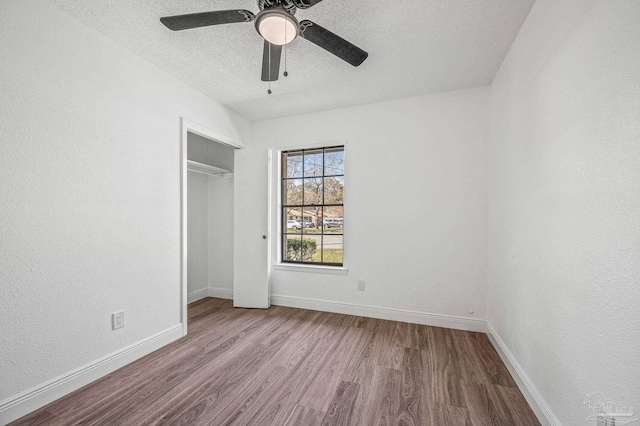 unfurnished bedroom featuring wood finished floors, baseboards, ceiling fan, a closet, and a textured ceiling