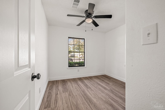 empty room featuring visible vents, a textured ceiling, wood finished floors, baseboards, and ceiling fan