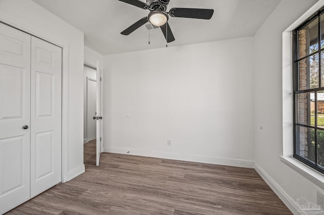 unfurnished bedroom with dark wood finished floors, baseboards, a closet, and ceiling fan