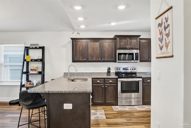 kitchen with light stone countertops, appliances with stainless steel finishes, dark brown cabinetry, and sink