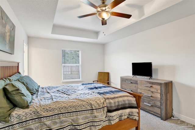 carpeted bedroom with a raised ceiling and ceiling fan