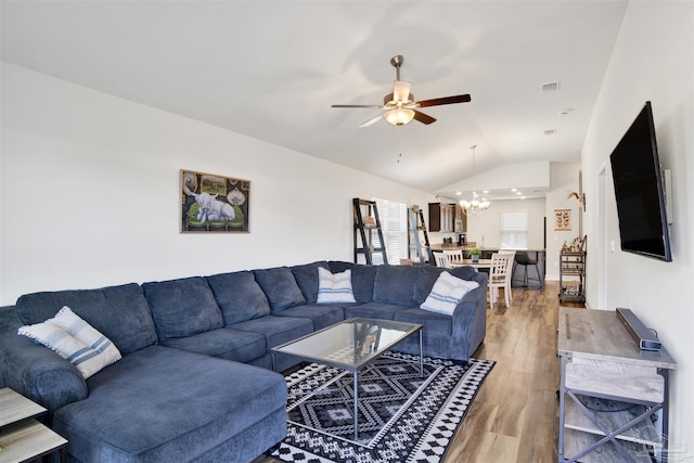 living room with ceiling fan with notable chandelier, wood-type flooring, and vaulted ceiling