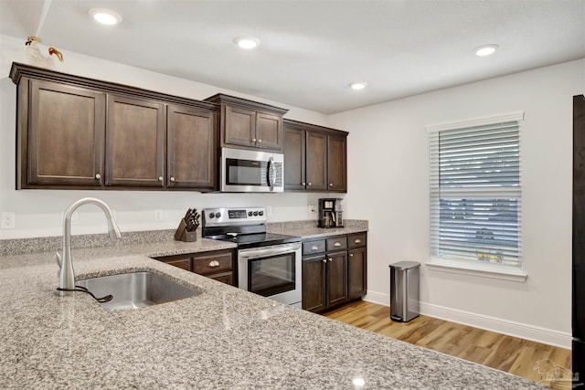 kitchen with appliances with stainless steel finishes, light stone counters, dark brown cabinets, sink, and light hardwood / wood-style floors