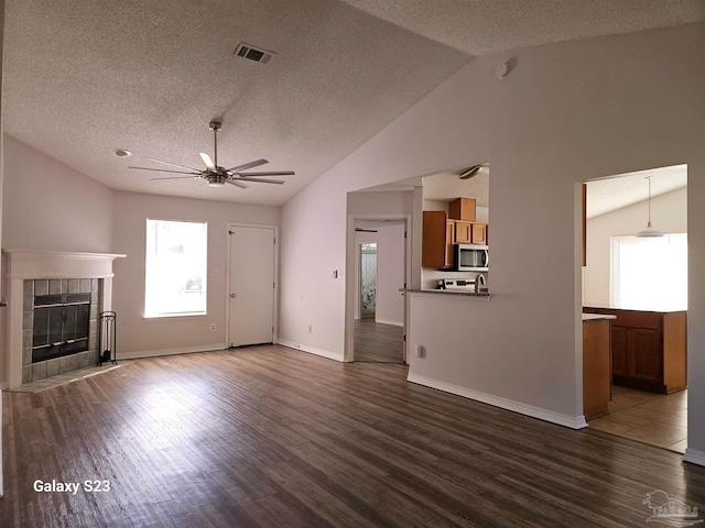 unfurnished living room with ceiling fan, a textured ceiling, vaulted ceiling, a tiled fireplace, and hardwood / wood-style flooring