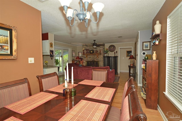 5845 Keystone Rd, Pensacola, FL 32504 - dining area featuring a chandelier, light wood-style flooring, a textured ceiling, a stone fireplace, and a ceiling fan