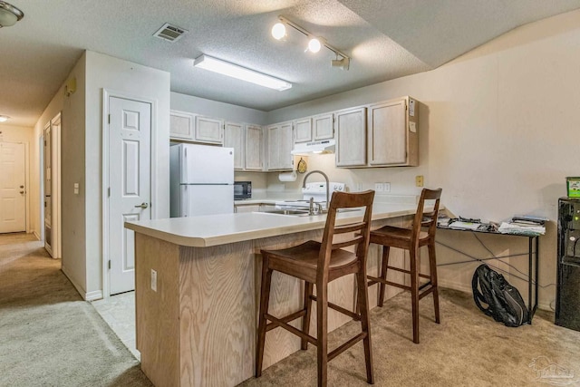 kitchen with white refrigerator, kitchen peninsula, light colored carpet, a textured ceiling, and light brown cabinetry