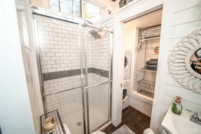 bathroom featuring wood-type flooring, stacked washer and dryer, walk in shower, and sink