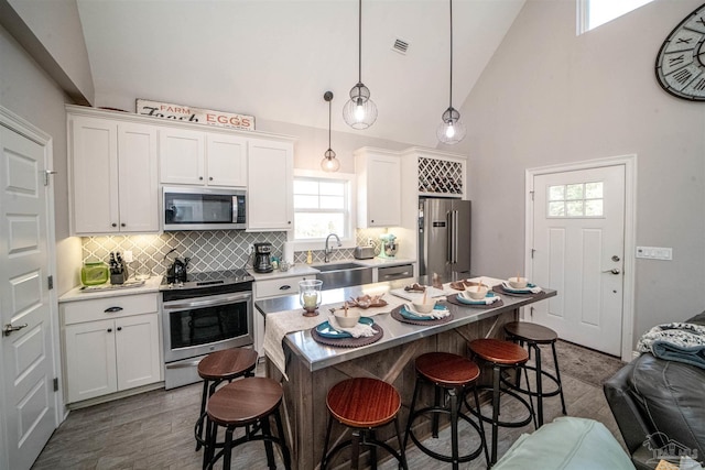 kitchen with decorative backsplash, stainless steel appliances, sink, white cabinets, and hanging light fixtures