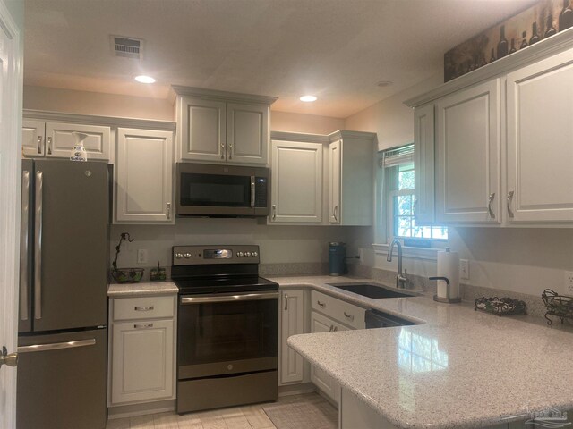 kitchen with kitchen peninsula, sink, white cabinets, appliances with stainless steel finishes, and light stone counters